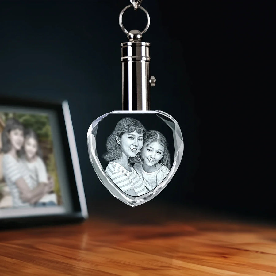 Heart-shaped crystal keychain with engraved photo of a mother and child on a wooden surface.
